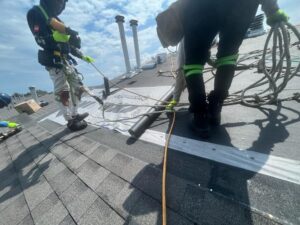 Roofers wearing safety harnesses installing underlayment and shingles on a sloped roof