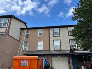 Roofing crew re-roofing a three-storey townhouse with a disposal bin in the driveway